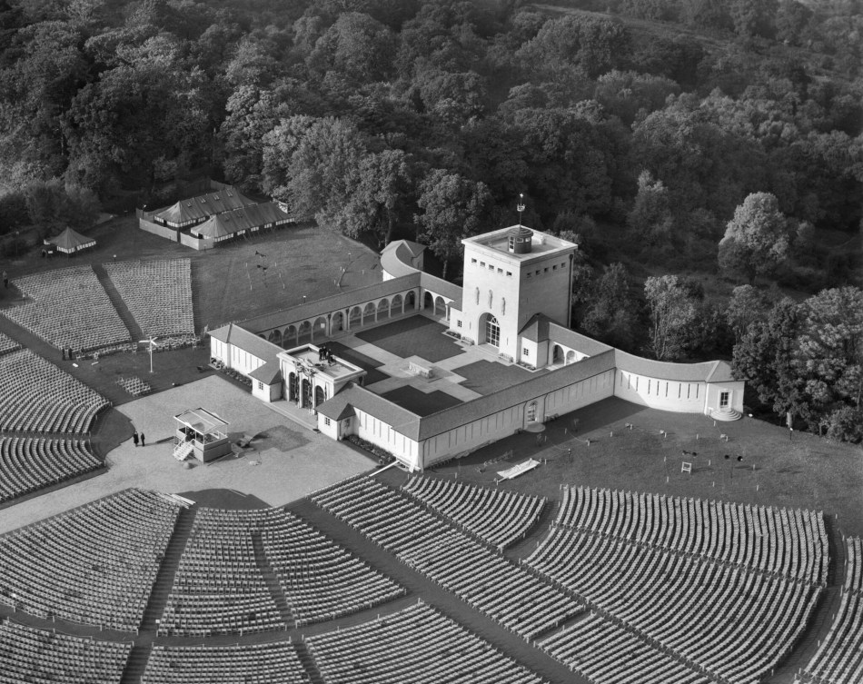 A black and white aerial photograph of a large memorial set out in a quadrangular plan, with rows of seats set up in front of the entrance.