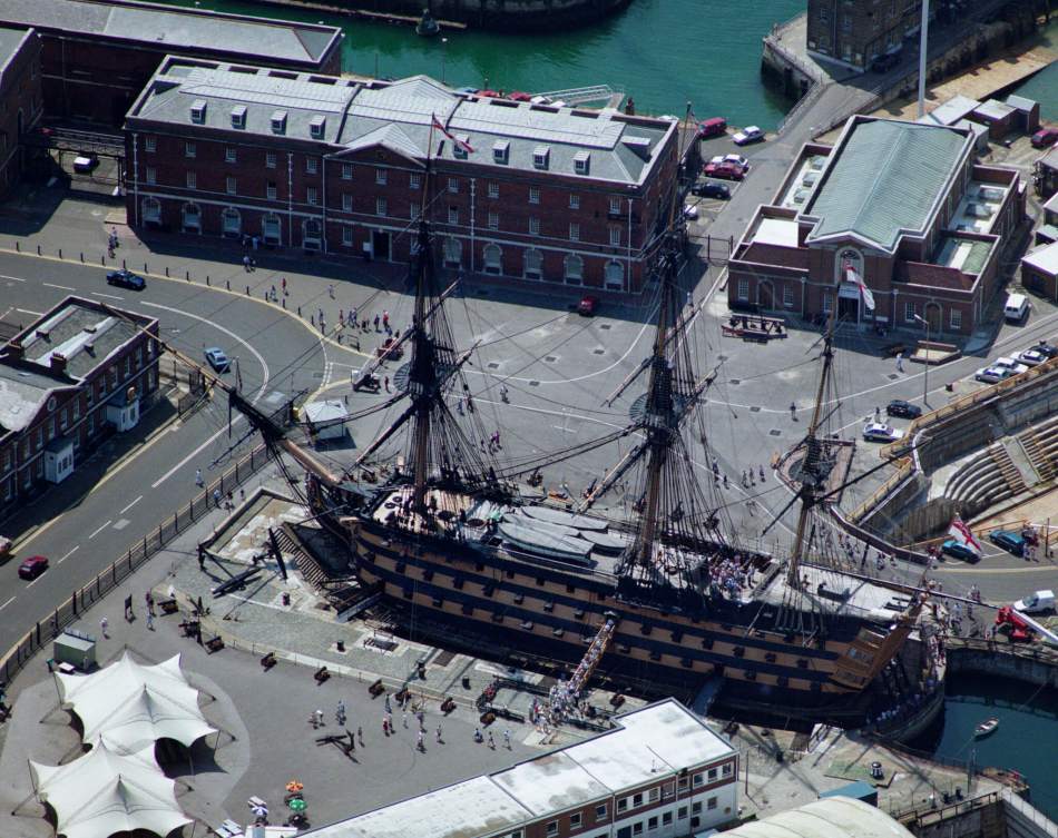 An aerial photograph of a large, 18th-century ship in a dockyard.