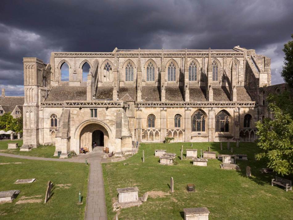 A photograph of the exterior of an abbey with a graveyard in front of the entrance.