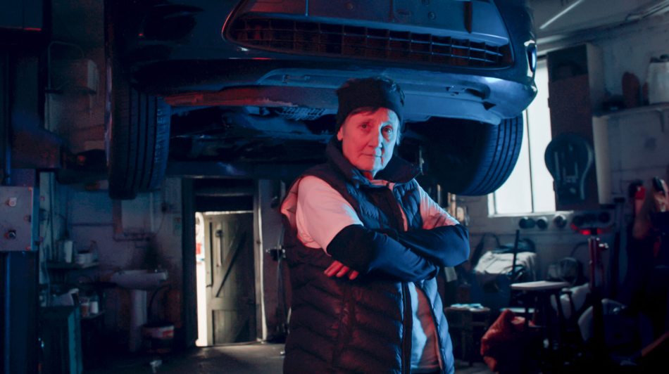 A photograph of a woman standing with her arms crossed in a garage.