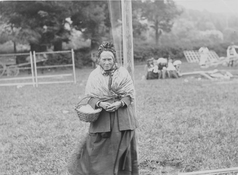 A black and white photograph of a Gypsy woman holding a basket. 