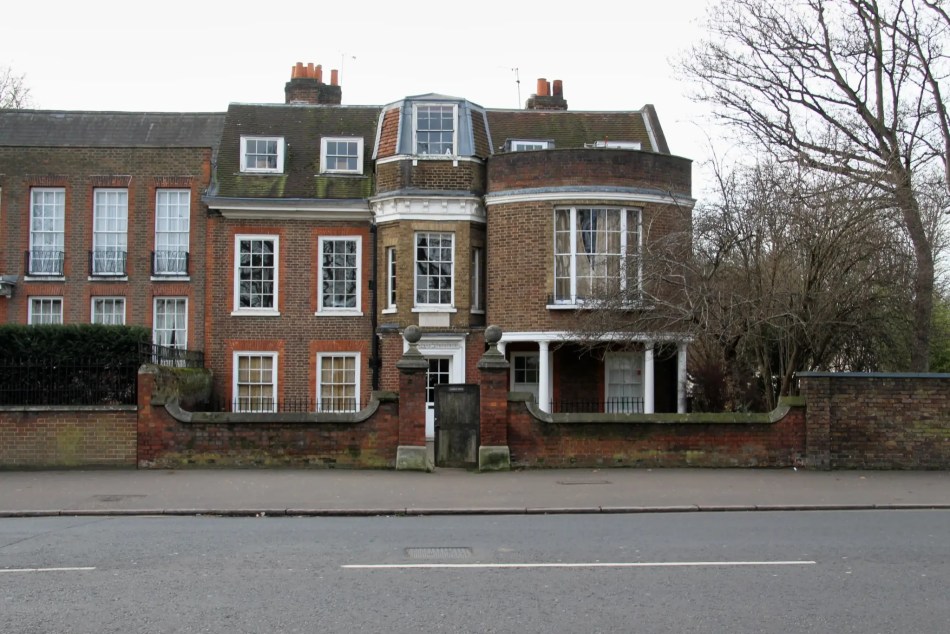 A photograph of the exterior of a large, 3-storey, 18th-century brick building with a boundary wall in front of the entrance.