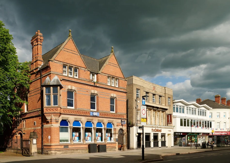 A colour photograph of a large red brick building against a moody sky. 