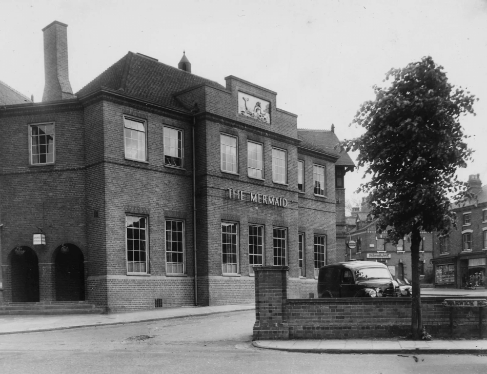 A black and white photograph of a public house. A sign on the building reads: 'THE MERMAID'