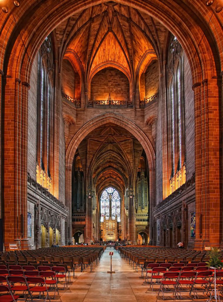 Interior of a cathedral looking up the main aisle towards the alter and distant stained glass window behind it.