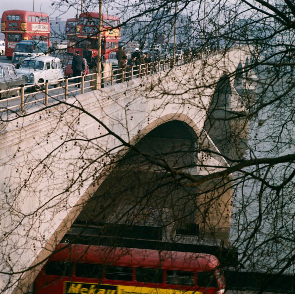 Oblique view of Waterloo Bridge in heavy traffic in 1959, with a double-decker bus passing along the Victoria Embankment below the bridge in the foreground.